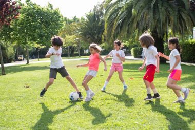 Group of kids enjoying a game of soccer in a lush green park on a sunny day in Portugal.