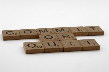 Scrabble tiles spelling 'Commit Or Quit' on a white surface, symbolizing decision-making.